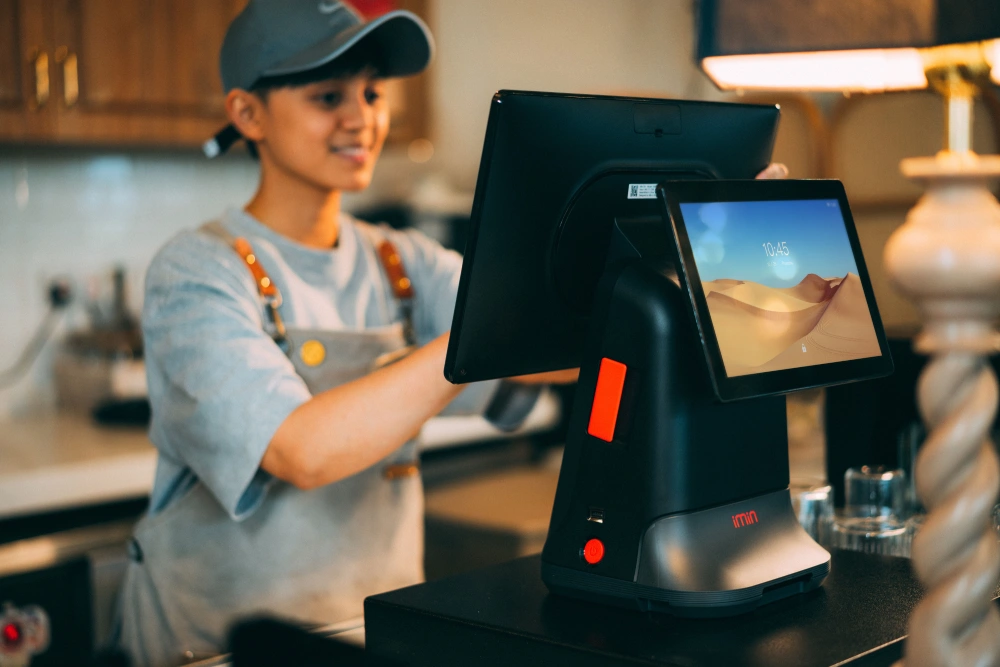 A restaurant employee interacting with a dual-screen cloud POS system at a counter, showcasing how modern cloud-based point of sale hardware connects a business.