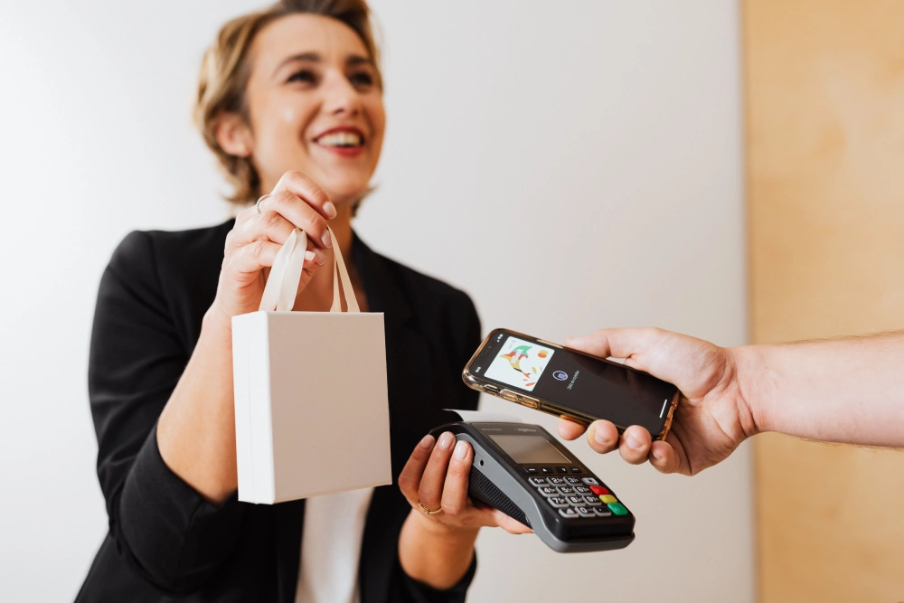 A customer using a smartphone to complete a contactless payment on a mobile POS terminal held by a smiling retail employee.